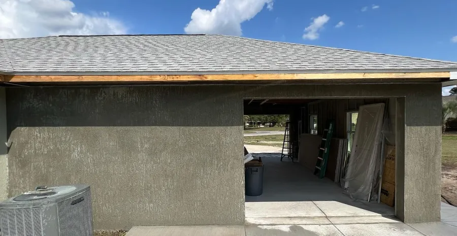 Gray stucco exterior walls with open garage under gray shingled roof at residential construction site
